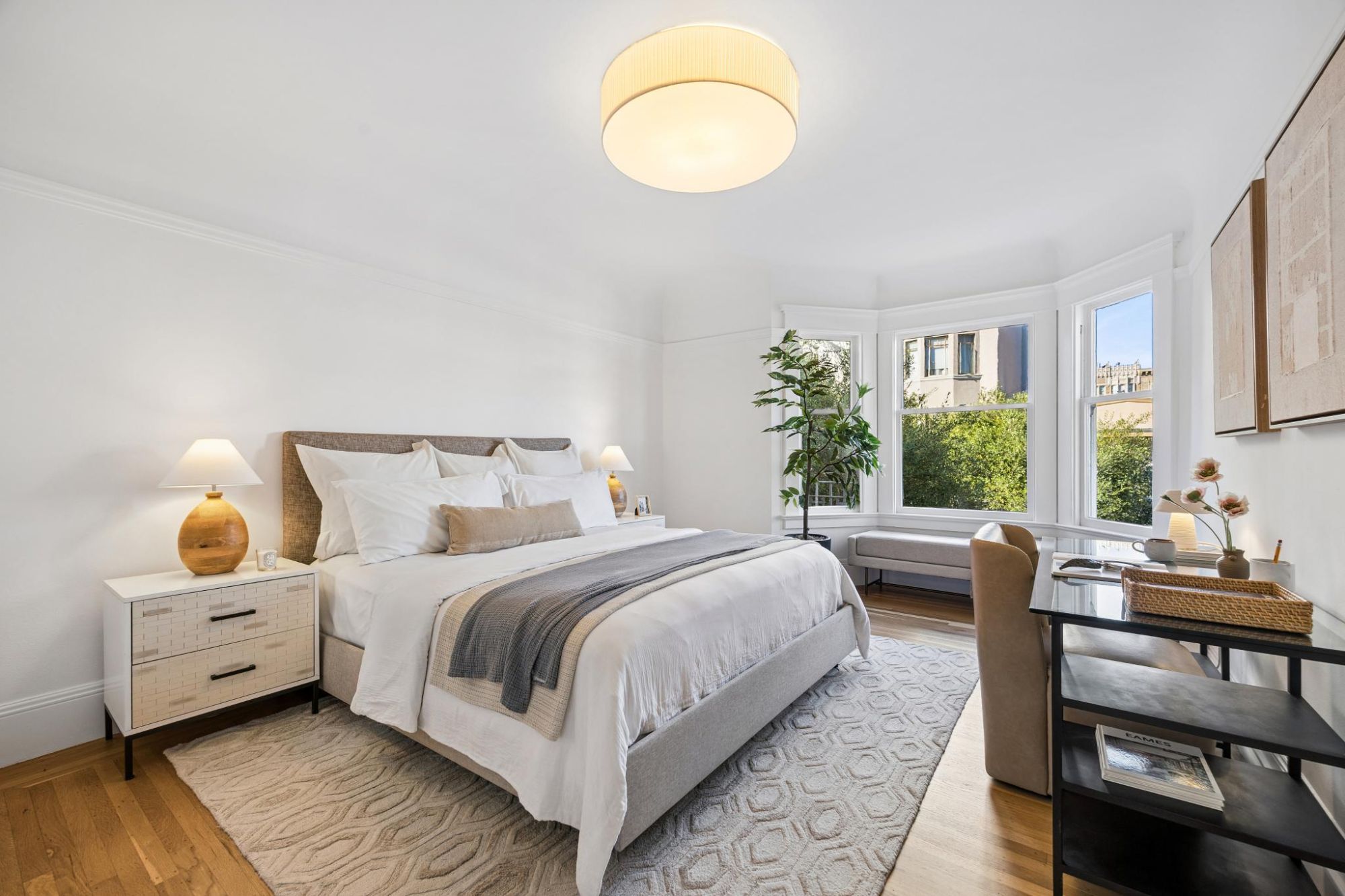 Second bedroom with a bay window onto trees, a queen bed, and a desk