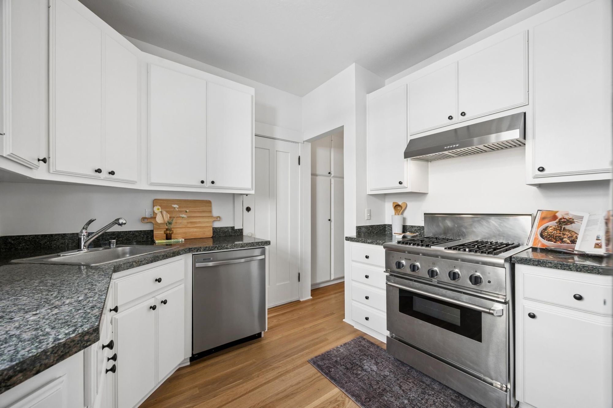 Kitchen with white cabinets, dark granite counters, a stainless dishwasher, and a stainless gas range with hood