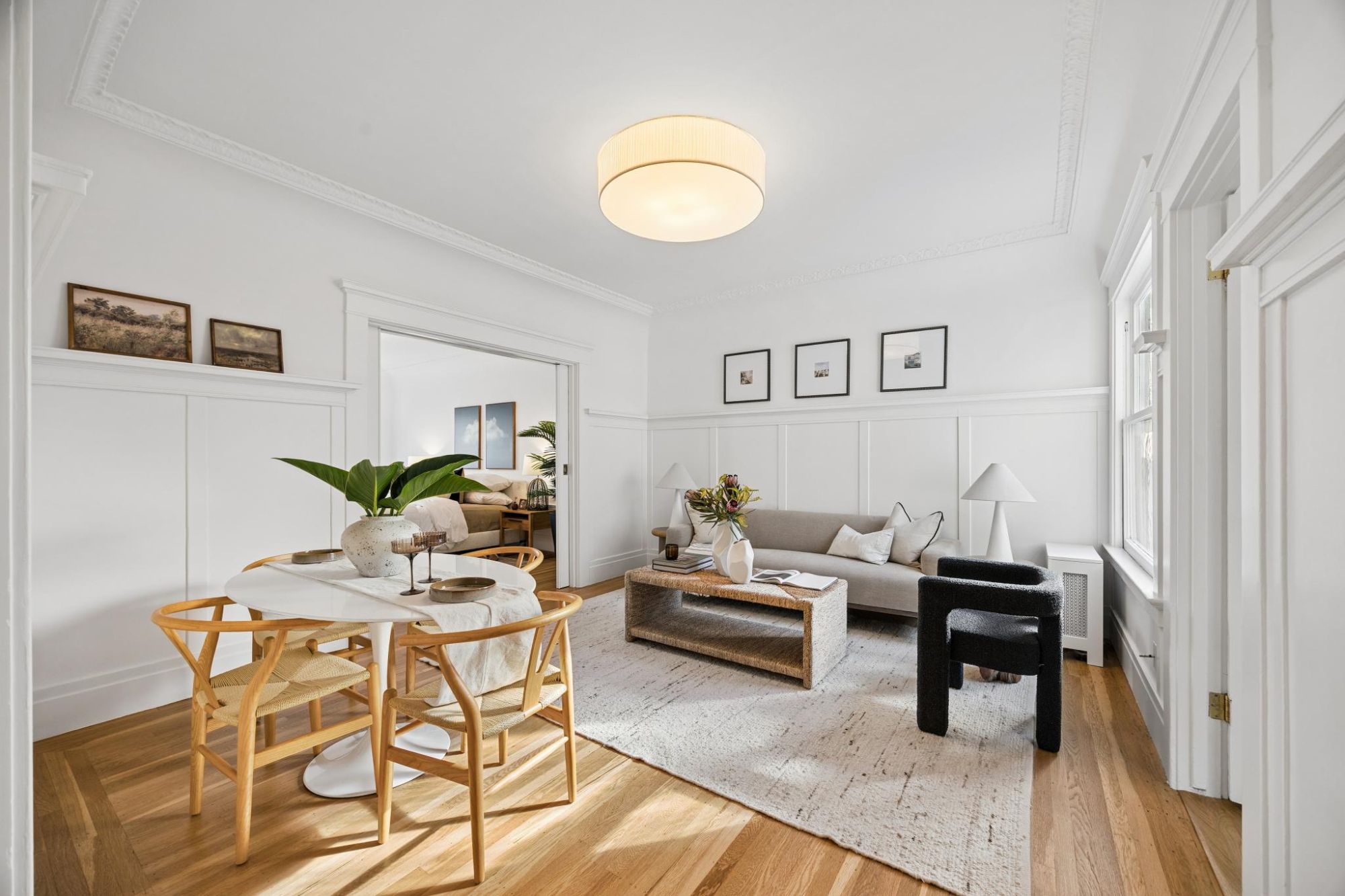 Living and dining area with a round white dining table, wishbone chairs, a sofa, and pocket doors open to a bedroom